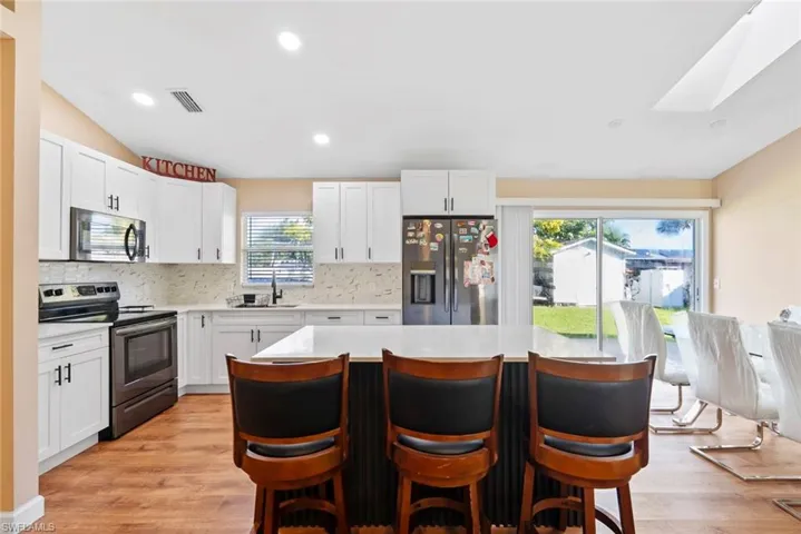 White cabinetry, stainless steel appliances, wood-finish flooring, island with countertop seating, and sliding glass doors