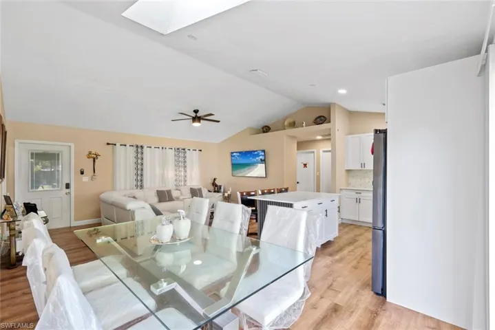 Vaulted ceiling, recessed lighting, wood-finish flooring, white kitchen cabinetry, and a kitchen island
