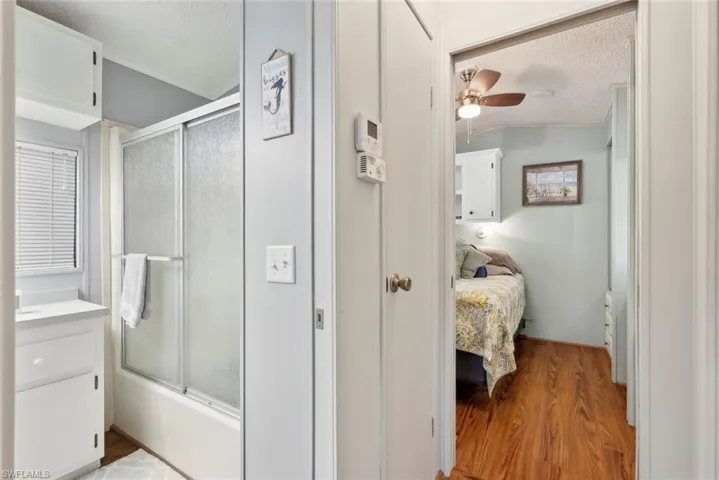 Bathroom with vanity, enclosed tub / shower combo, ceiling fan, wood-type flooring, and vaulted ceiling