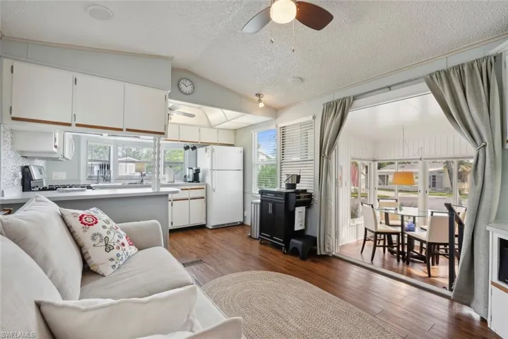 Living room with ceiling fan, wood-type flooring, vaulted ceiling, and a textured ceiling