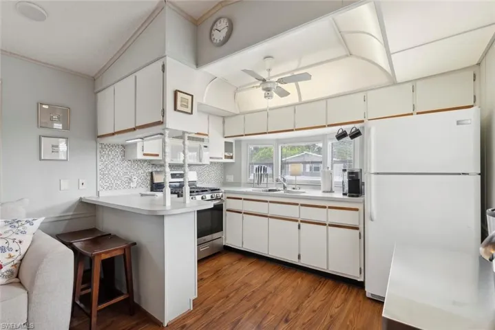 Kitchen with white appliances, white cabinetry, backsplash, ceiling fan, and hardwood / wood-style floors
