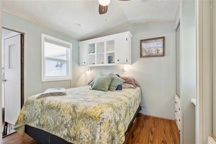 Bedroom with ceiling fan, a textured ceiling, dark hardwood / wood-style floors, and lofted ceiling