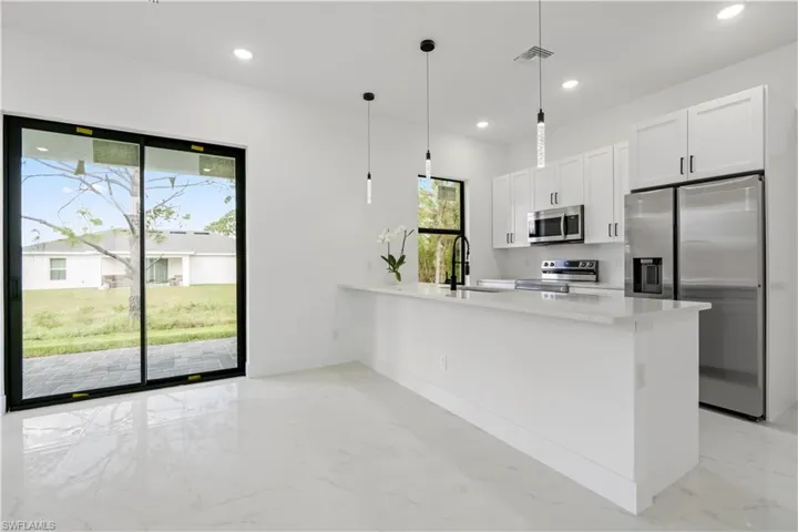 Kitchen featuring pendant lighting, white cabinets, sink, light stone countertops, and appliances with stainless steel finishes