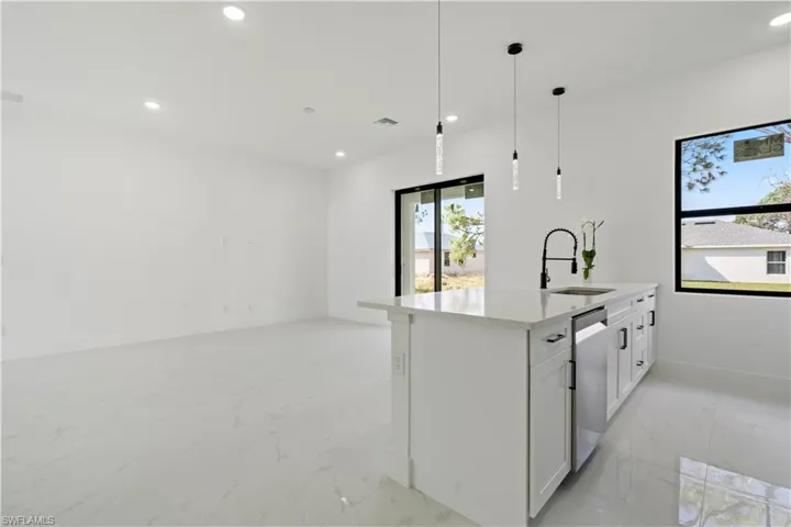 Kitchen featuring dishwasher, white cabinets, a center island with sink, sink, and decorative light fixtures