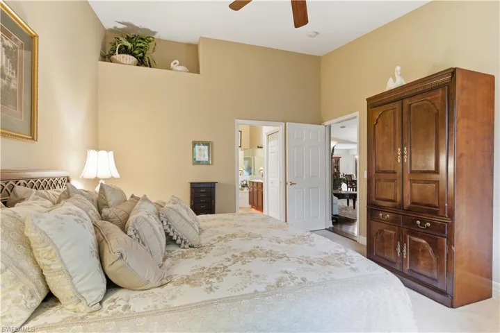 Bedroom with light colored carpet, ceiling fan, connected bathroom, and a high ceiling