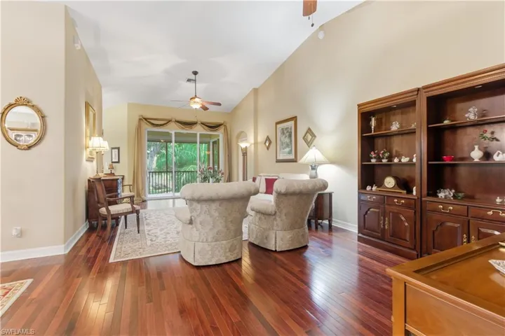 Living area with dark wood-style flooring, a ceiling fan, and lofted ceiling