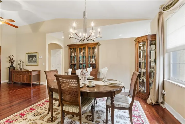 Dining area featuring dark wood-style flooring, lofted ceiling, a chandelier, arched walkways, and ceiling fan