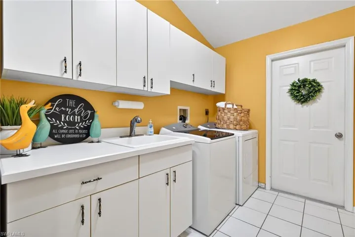 Laundry area featuring light tile patterned flooring, cabinet space, washing machine and dryer.