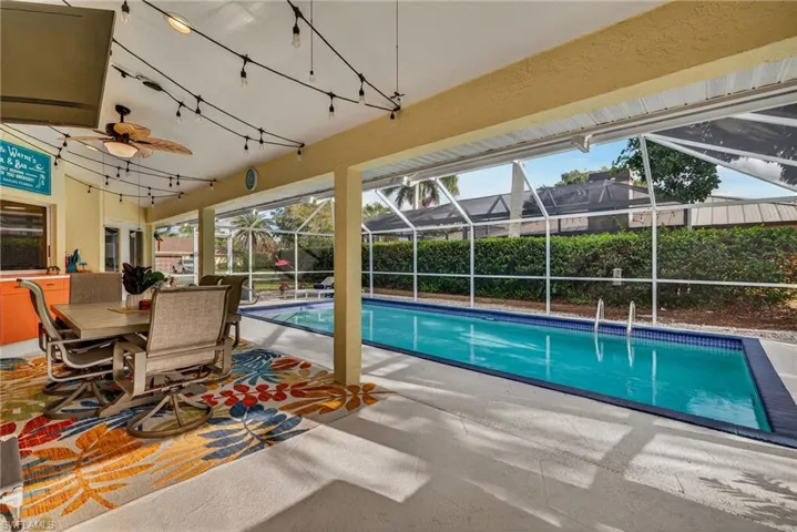 View of swimming pool with patio surround, outdoor dining space, a sunroom, and a lanai