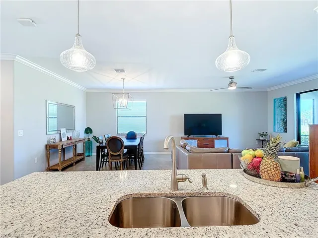 Kitchen with sink, light stone countertops, ceiling fan, crown molding, and pendant lighting