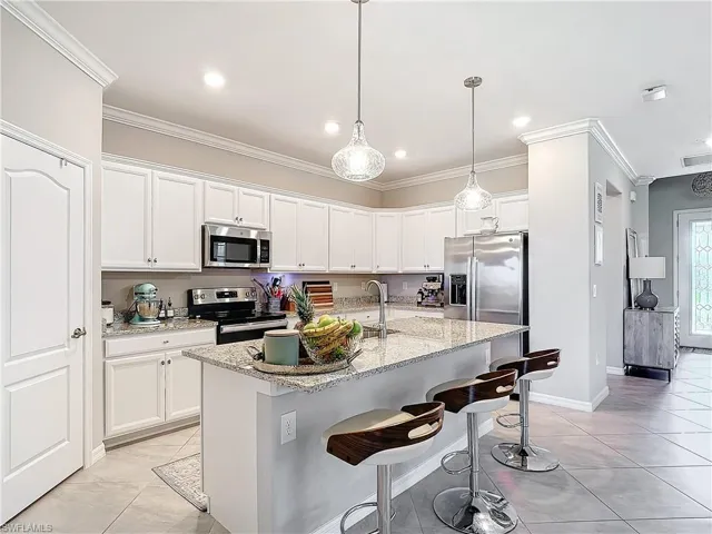 Kitchen featuring white cabinetry, appliances with stainless steel finishes, light stone countertops, a kitchen island with sink, and crown molding
