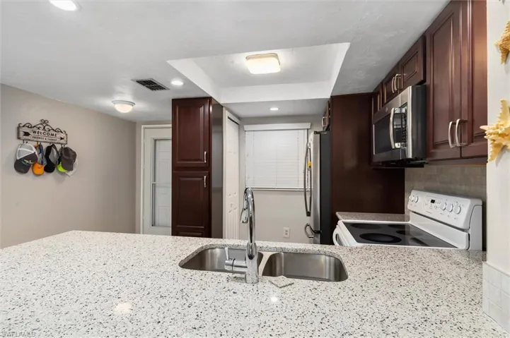 Kitchen featuring light stone countertops, sink, stainless steel appliances, and decorative backsplash