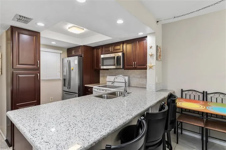 Kitchen with kitchen peninsula, light stone countertops, light tile patterned flooring, backsplash, and stainless steel appliances