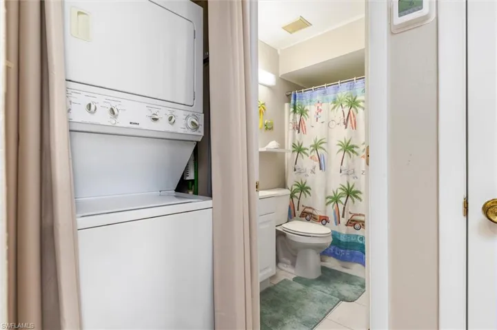 Laundry room with stacked washer and clothes dryer and light tile patterned floors