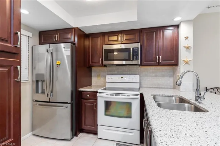 Kitchen featuring tasteful backsplash, light tile patterned flooring, appliances with stainless steel finishes, light stone countertops, and sink