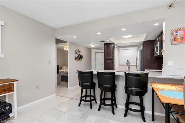 Kitchen featuring appliances with stainless steel finishes, kitchen peninsula, light stone countertops, light tile patterned floors, and a breakfast bar area