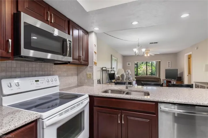 Kitchen featuring tasteful backsplash, ceiling fan with notable chandelier, stainless steel appliances, light stone countertops, and sink