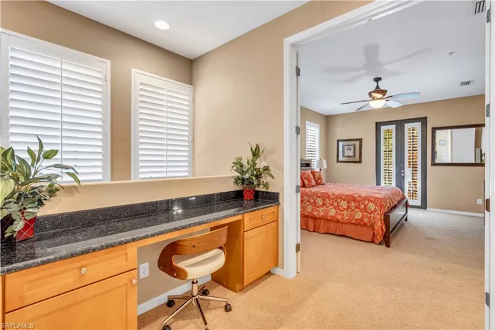 Built-in desk featuring stone-finish countertops, natural wood cabinetry, plantation shutters, and recessed lighting