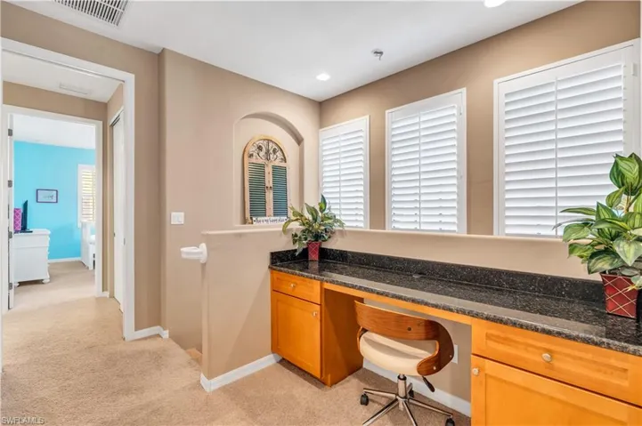 Built-in desk featuring stone-finish countertops, wood-finish cabinetry, recessed wall niche, and plantation shutters