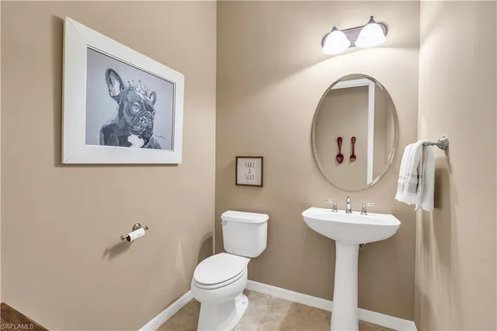 White pedestal sink with chrome faucet, oval wall-mounted mirror, two-light fixture with glass shades, and tile flooring