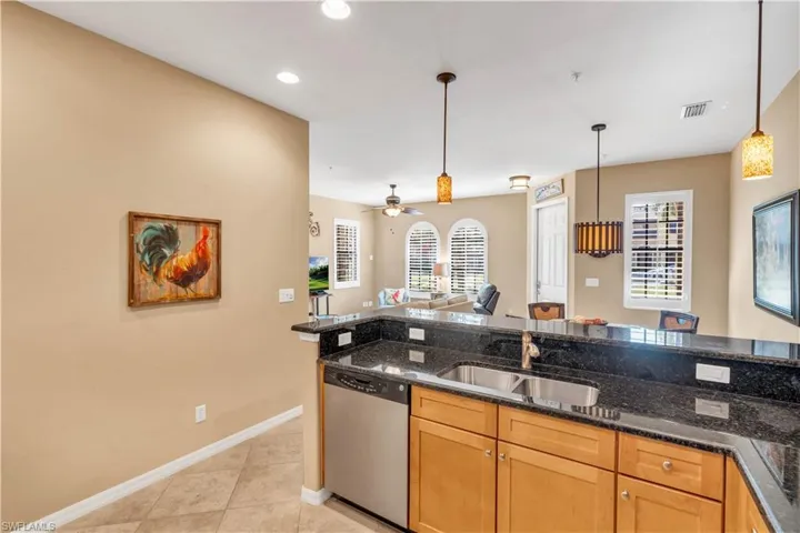 Kitchen featuring stone-finish countertops, stainless steel dishwasher, double-basin undermount sink, light-finish cabinetry, and pendant lighting
