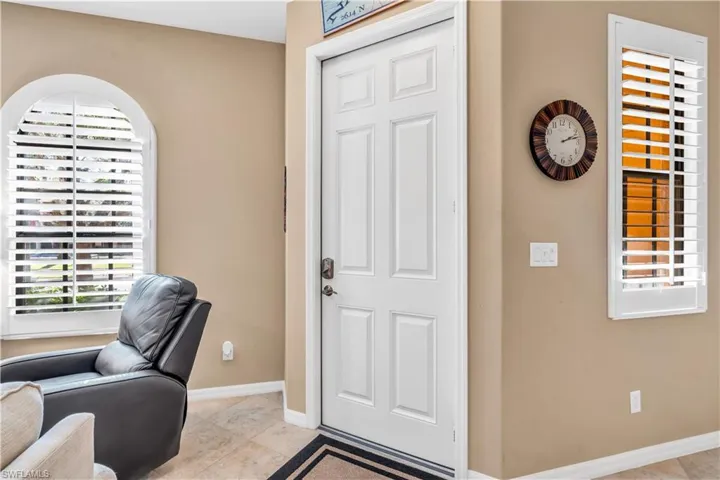 Entryway featuring a white six-panel door, arched window, plantation shutters, and neutral stone-finish tile flooring