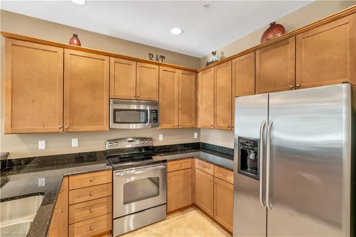 Kitchen featuring medium-tone wood cabinetry, dark stone countertops, stainless steel appliances, a built-in microwave, and recessed lighting