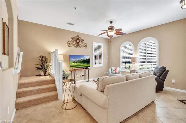 Living area featuring arched windows with plantation shutters, tile flooring, and a ceiling fan with integrated lighting