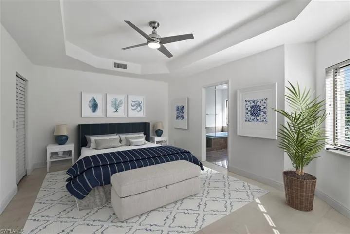 Bedroom with a raised ceiling, ensuite bathroom, and ceiling fan