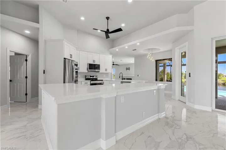 Kitchen featuring white cabinetry, ceiling fan, stainless steel appliances, light tile patterned floors, and a spacious island
