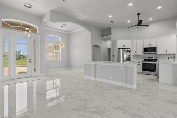 Kitchen with appliances with stainless steel finishes, sink, decorative light fixtures, light tile patterned floors, and a towering ceiling