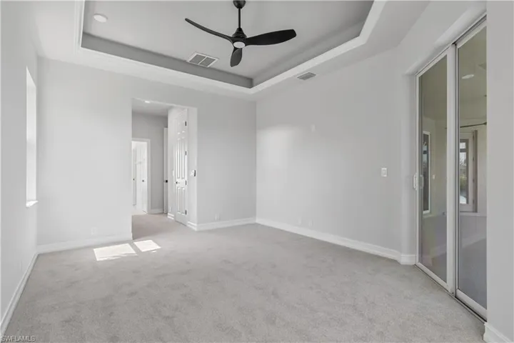 Carpeted empty room featuring ceiling fan and a raised ceiling