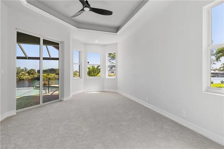 Empty room with carpet floors, a tray ceiling, a water view, and ceiling fan