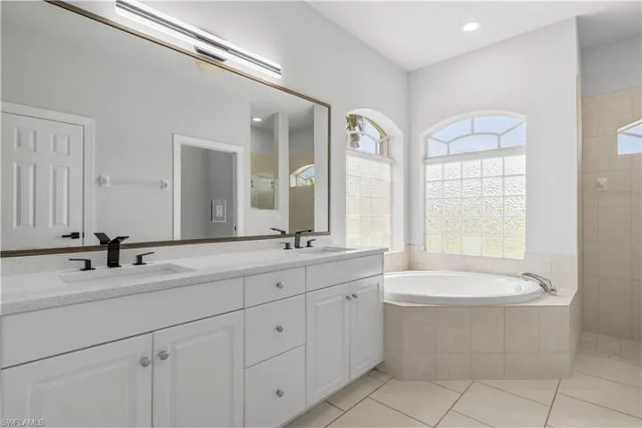 Bathroom featuring dual vanity, tile patterned flooring, and tiled bath