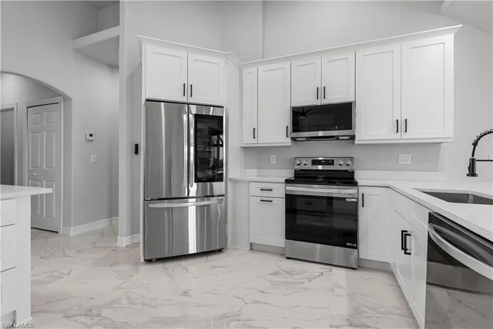 Kitchen with sink, a towering ceiling, stainless steel appliances, and white cabinetry