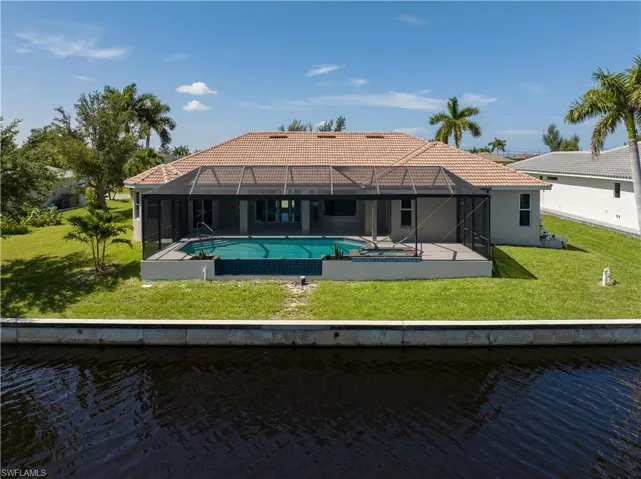Back of house with a water view, a lawn, and glass enclosure