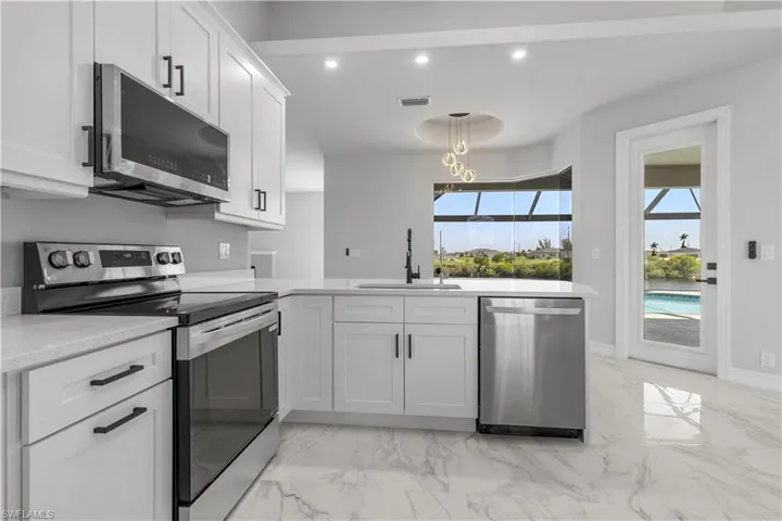 Kitchen featuring light tile patterned floors, white cabinets, stainless steel appliances, decorative light fixtures, and sink
