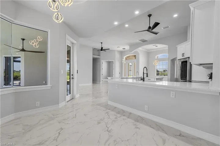 Kitchen with light tile patterned flooring, white cabinets, light stone counters, ceiling fan, and stainless steel fridge
