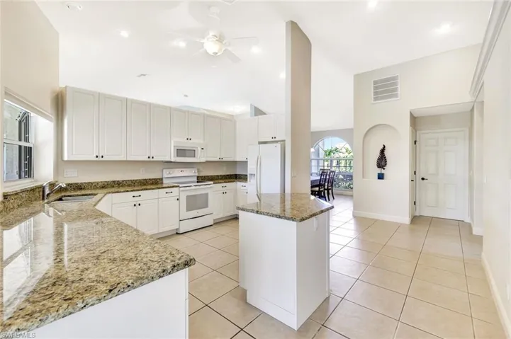 Kitchen featuring white appliances, a sink, dark stone counters, vaulted ceiling, and ceiling fan