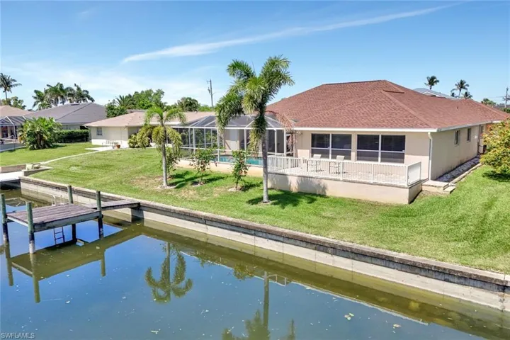 Rear view of house with a water view, a yard, a shingled roof, glass enclosure, and stucco siding