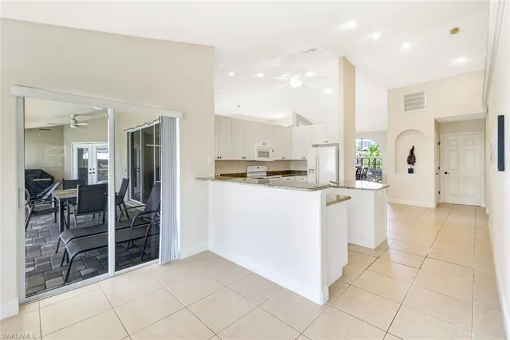 Kitchen featuring white appliances, a ceiling fan, light tile patterned floors, a peninsula, and high vaulted ceiling