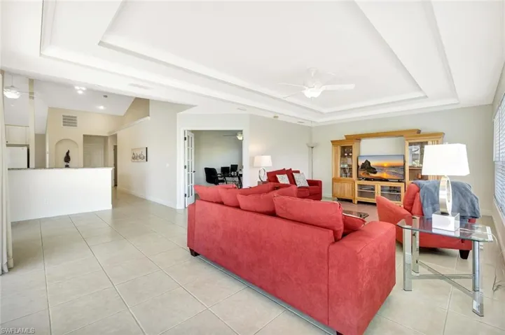 Living area featuring a tray ceiling, a ceiling fan, light tile patterned flooring, and baseboards