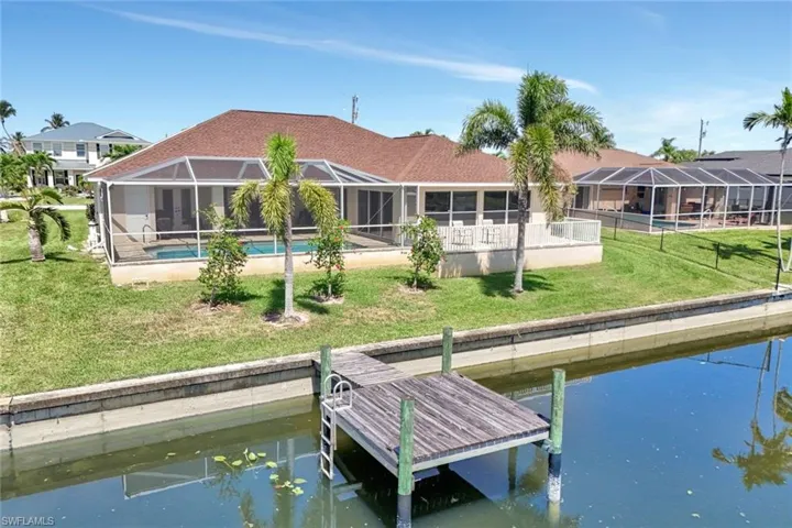 Rear view of house with a water view, a yard, an outdoor pool, and glass enclosure