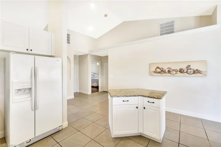 Kitchen featuring white refrigerator with ice dispenser, light tile patterned flooring, white cabinets, baseboards, and high vaulted ceiling