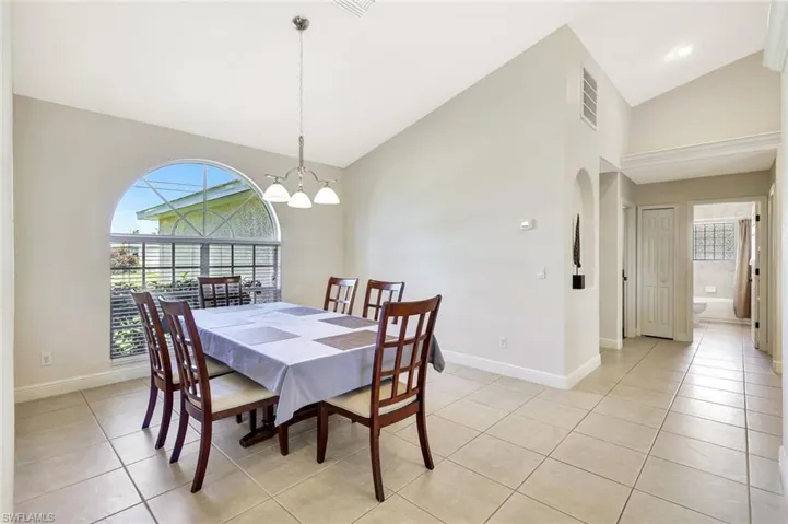Dining area with high vaulted ceiling, baseboards, light tile patterned flooring, a chandelier, and arched walkways