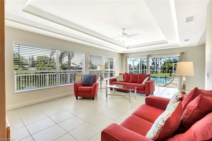 Living area featuring a tray ceiling, ceiling fan, light tile patterned floors, and baseboards
