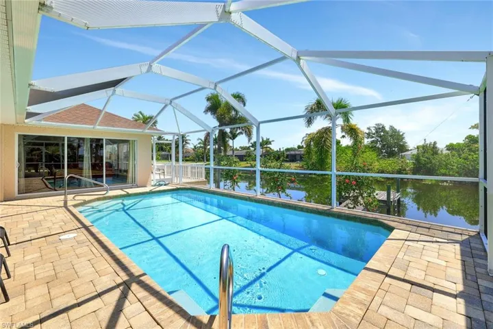 Outdoor pool featuring a patio, a water view, and glass enclosure