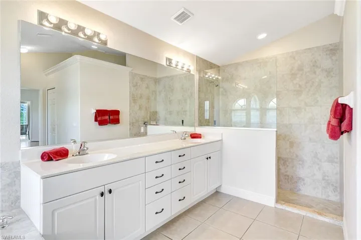 Full bathroom with vaulted ceiling, tile patterned flooring, double vanity, and walk in shower