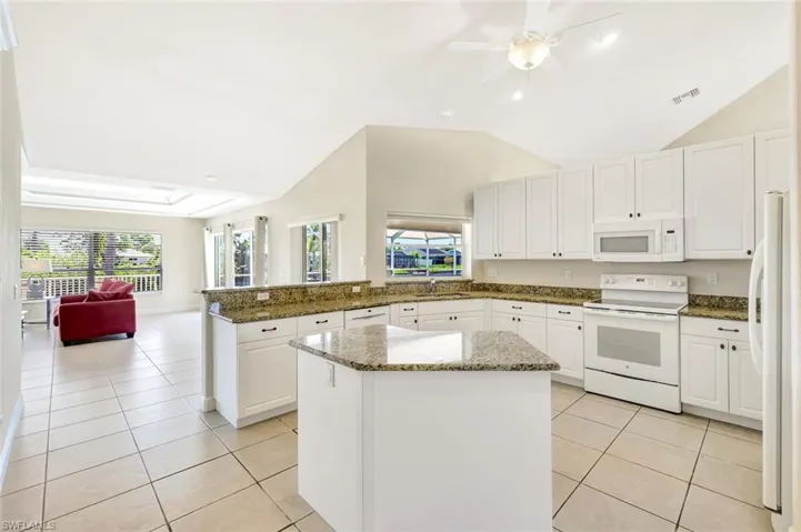 Kitchen featuring white appliances, a peninsula, light tile patterned floors, a sink, and a center island