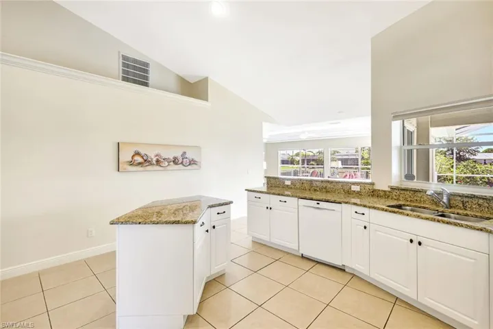 Kitchen with white dishwasher, a sink, light tile patterned flooring, stone counters, and high vaulted ceiling